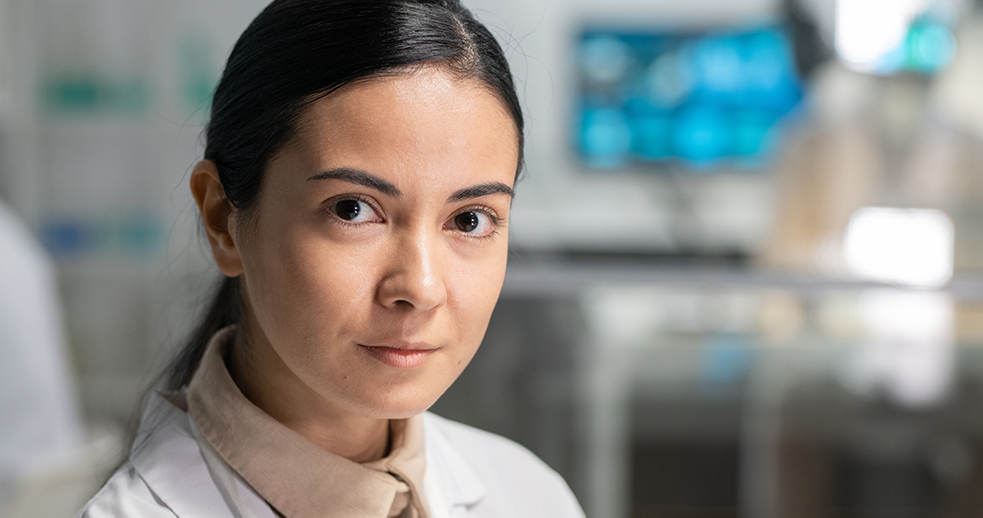 A young woman researcher in a white lab coat looking at the camera