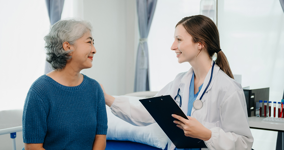 A young woman doctor talking with a patient on a hospital bed.
